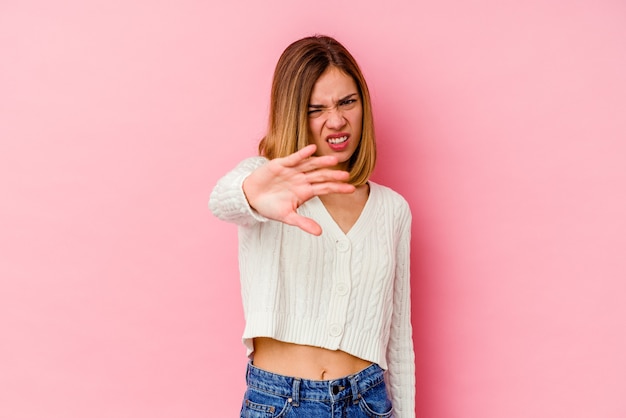 Jovem mulher caucasiana isolada na rosa rejeitando alguém mostrando um gesto de nojo.