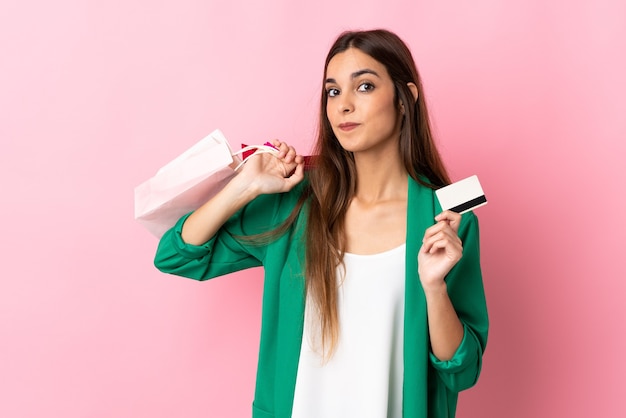 Jovem mulher caucasiana isolada na rosa segurando sacolas de compras e um cartão de crédito