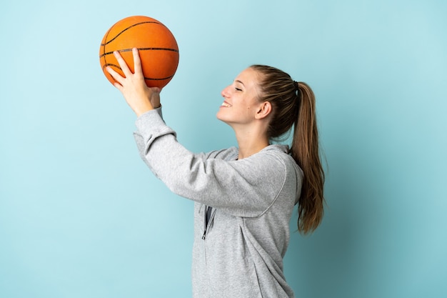 Jovem mulher caucasiana isolada no azul jogando basquete