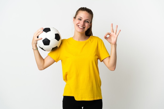 Jovem mulher caucasiana isolada no branco com bola de futebol e fazendo sinal de ok