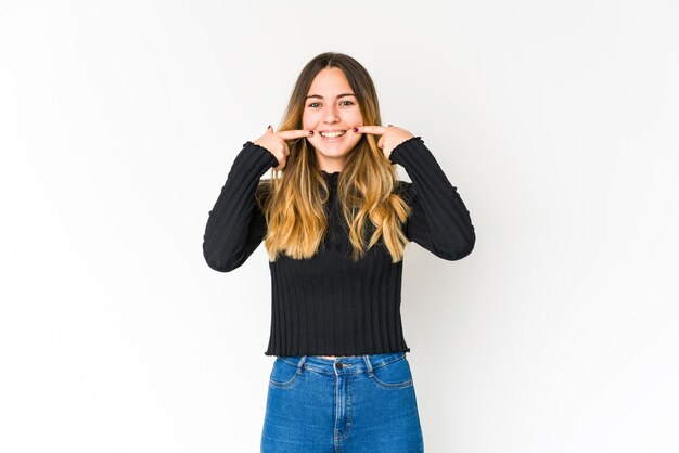 Jovem mulher caucasiana isolada no espaço em branco sorri, apontando o dedo para a boca.