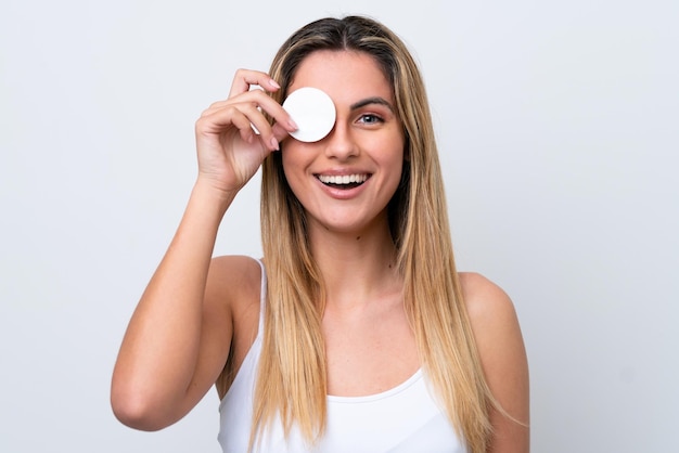 Jovem mulher caucasiana isolada no fundo branco com almofada de algodão para remover a maquiagem do rosto e sorrindo