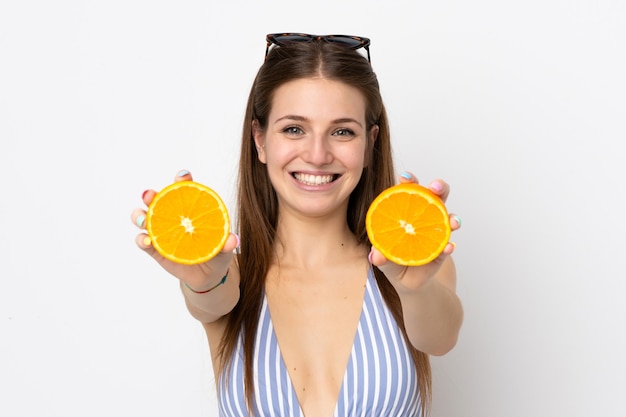 Foto jovem mulher caucasiana isolada no fundo branco, em traje de banho e segurando uma laranja