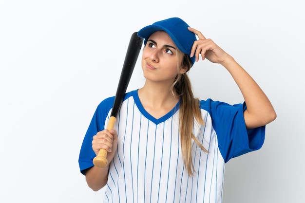 Jovem mulher caucasiana isolada no fundo branco jogando beisebol e tendo dúvidas com a expressão facial confusa