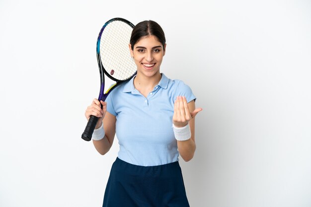 Jovem mulher caucasiana isolada no fundo branco jogando tênis e fazendo o gesto de aproximar-se