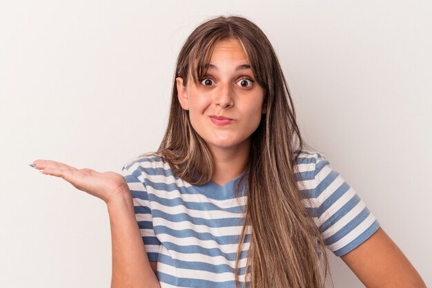 Jovem mulher caucasiana isolada no fundo branco, mostrando um espaço de cópia na palma da mão e segurando a outra mão na cintura.