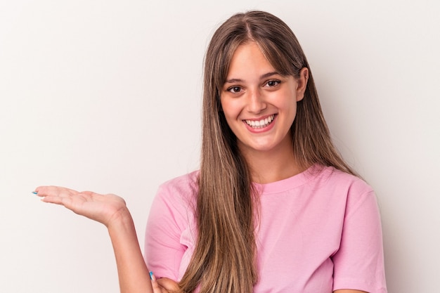 Jovem mulher caucasiana isolada no fundo branco, mostrando um espaço de cópia na palma da mão e segurando a outra mão na cintura.