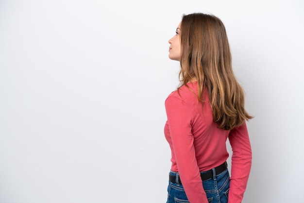 Foto jovem mulher caucasiana isolada no fundo branco na posição traseira e olhando para trás