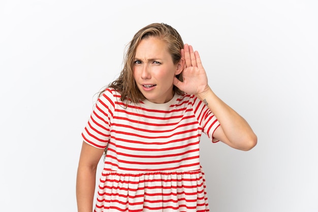 Foto jovem mulher caucasiana isolada no fundo branco ouvindo algo colocando a mão na orelha