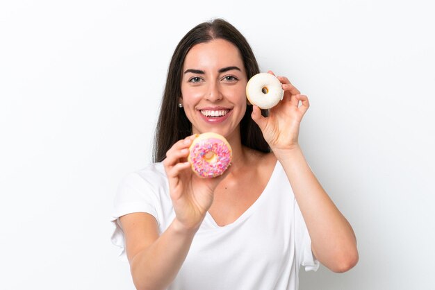 Jovem mulher caucasiana isolada no fundo branco segurando rosquinhas com uma expressão feliz