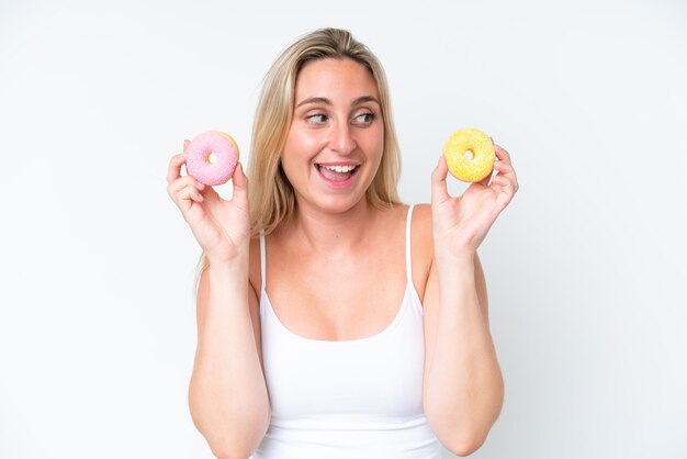 Jovem mulher caucasiana isolada no fundo branco segurando rosquinhas e surpresa