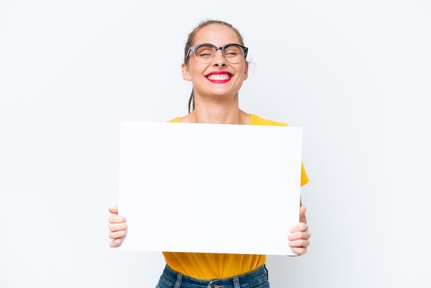 Jovem mulher caucasiana isolada no fundo branco segurando um cartaz vazio com expressão feliz