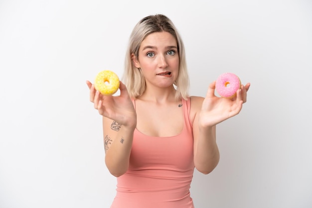 Foto jovem mulher caucasiana isolada no fundo branco segurando uma rosquinha e triste