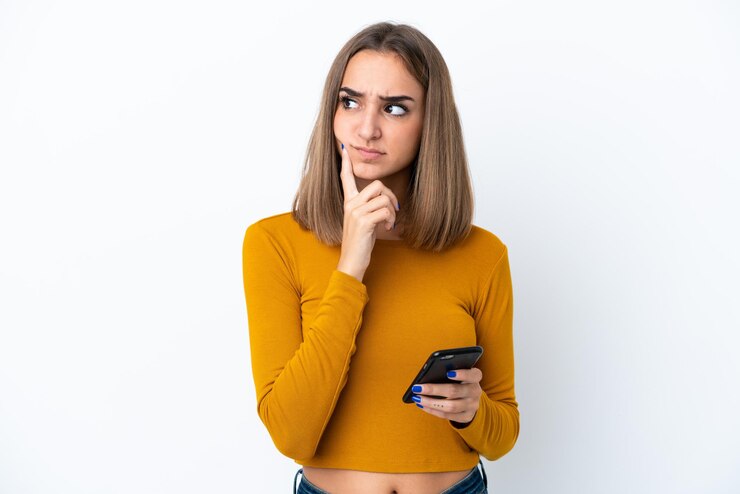 Foto jovem mulher caucasiana isolada no fundo branco usando telefone celular e pensando