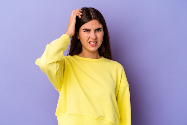 Jovem mulher caucasiana isolada no fundo roxo, esquecendo de algo, batendo na testa com a palma da mão e fechando os olhos.