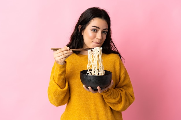 Foto jovem mulher caucasiana isolada segurando uma tigela de macarrão com pauzinhos