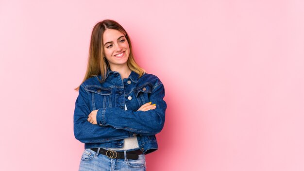 Jovem mulher caucasiana isolada sobre rosa sorridente coverfident com os braços cruzados.