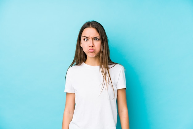 Jovem mulher caucasiana isolada sopra bochechas, tem expressão cansada. Conceito de expressão facial.