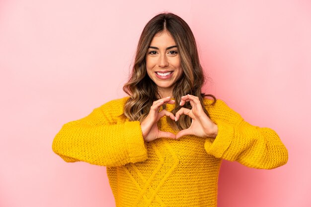 Jovem mulher caucasiana isolada sorrindo e mostrando uma forma de coração com as mãos.