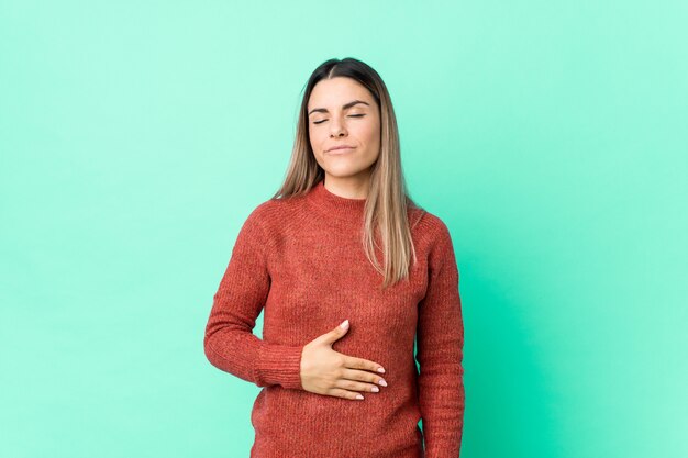 Jovem mulher caucasiana isolada toca a barriga, sorri suavemente, comendo e conceito de satisfação.