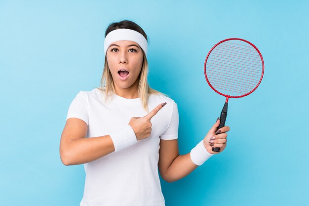 Jovem mulher caucasiana jogando badminton isolado apontando para o lado