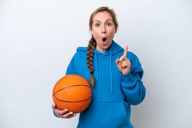 Jovem mulher caucasiana jogando basquete isolada no fundo branco com a intenção de perceber a solução enquanto levanta um dedo