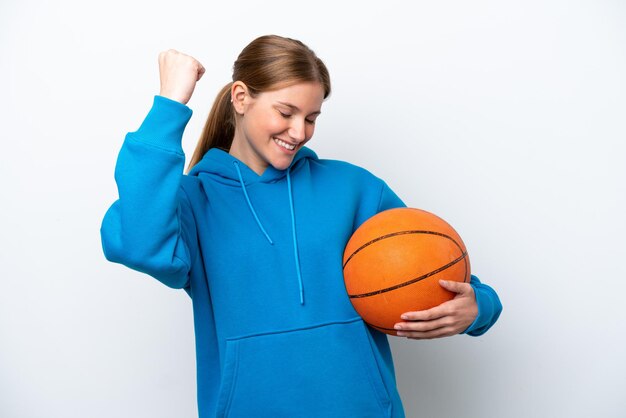 Jovem mulher caucasiana jogando basquete isolada no fundo branco comemorando uma vitória