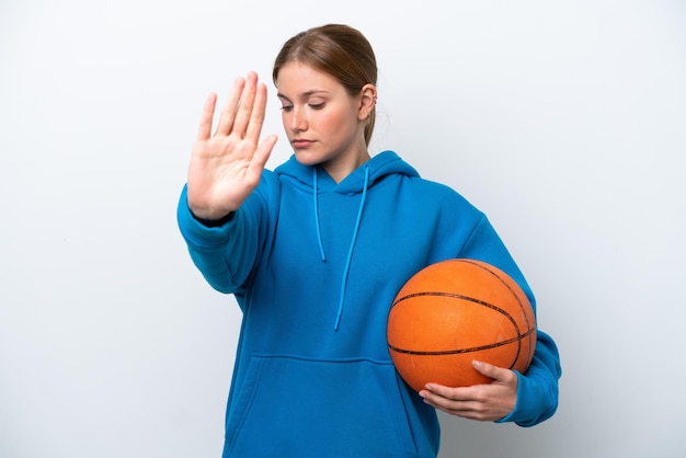 Jovem mulher caucasiana jogando basquete isolada no fundo branco fazendo gesto de parada e desapontada