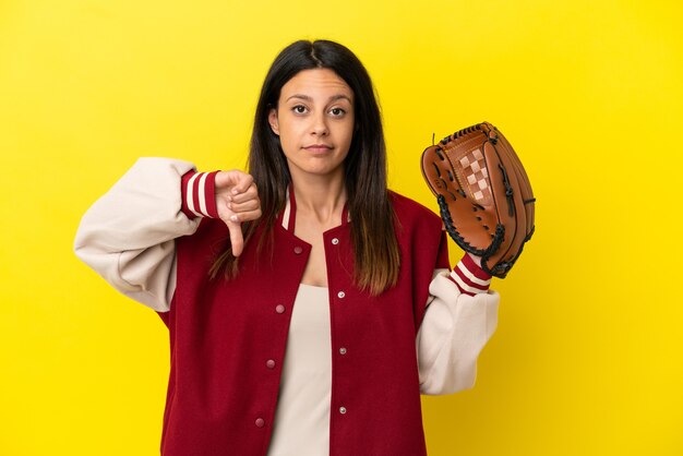 Jovem mulher caucasiana jogando beisebol isolado em um fundo amarelo, mostrando o polegar para baixo com expressão negativa