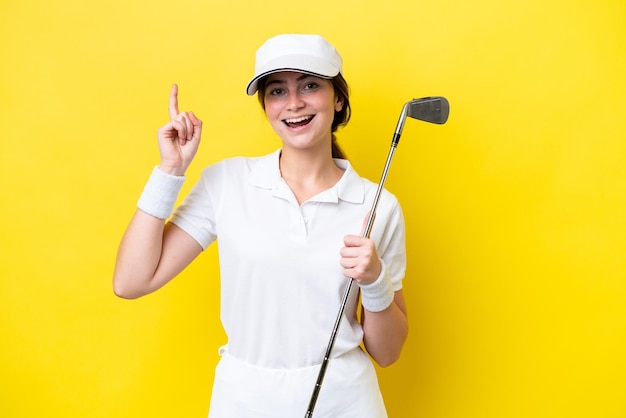 jovem mulher caucasiana jogando golfe isolado em fundo amarelo apontando uma grande ideia