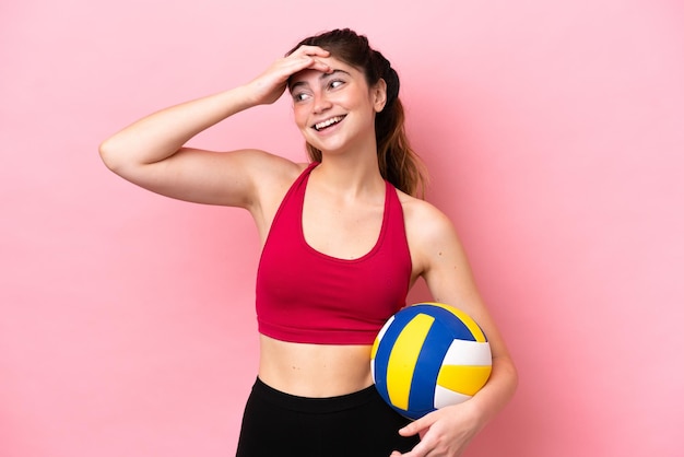 Jovem mulher caucasiana jogando vôlei isolada em fundo rosa sorrindo muito