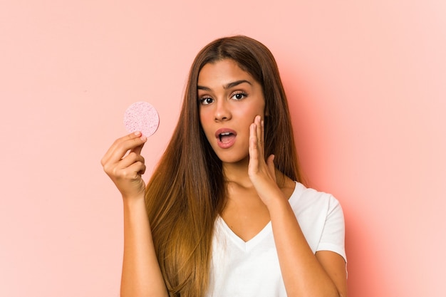 Jovem mulher caucasiana limpando o rosto com um disco facial isolado