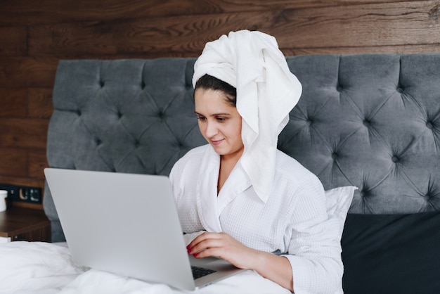 Jovem mulher caucasiana morena trabalhando em seu laptop na cama dela