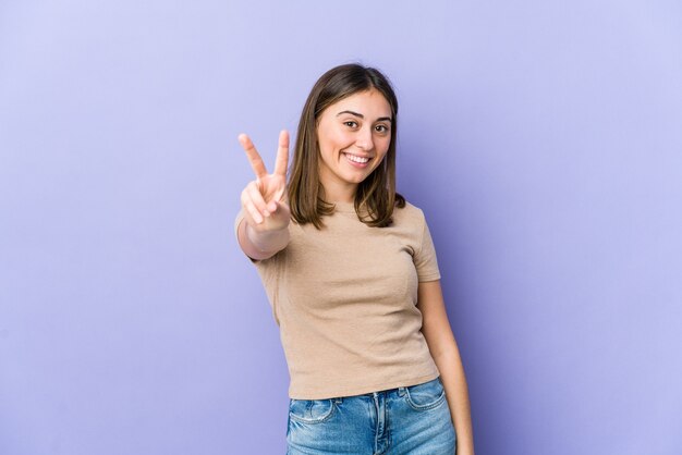 Jovem mulher caucasiana, mostrando sinal de vitória e sorrindo amplamente.