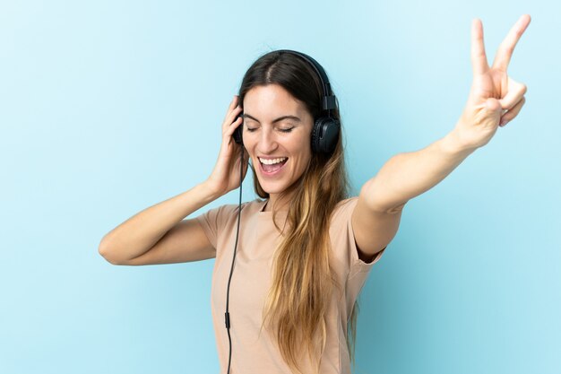 Jovem mulher caucasiana na parede azul, ouvir música e cantar