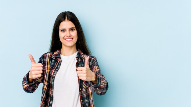 Jovem mulher caucasiana na parede azul, sorrindo e levantando o polegar