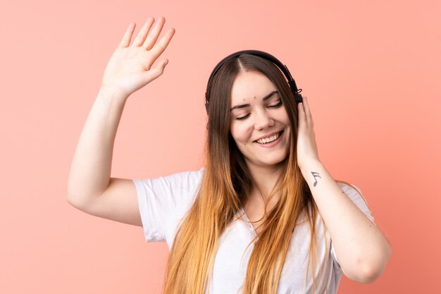 Jovem mulher caucasiana na parede rosa, ouvir música e dançar