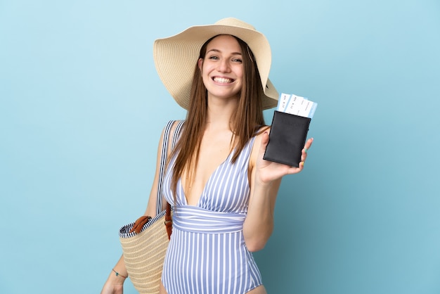 Jovem mulher caucasiana nas férias de verão segurando passaporte isolado em um fundo azul e sorrindo muito