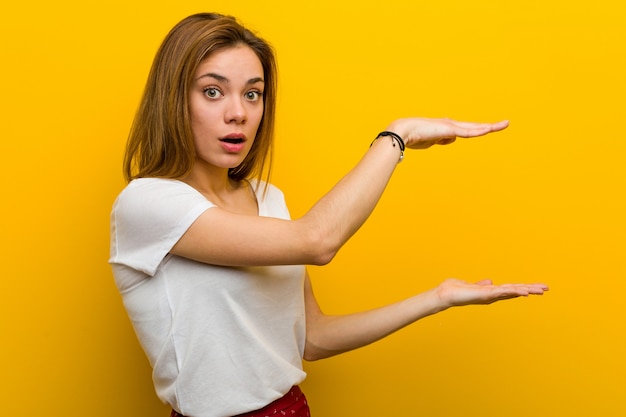 Jovem mulher caucasiana natural chocada e espantada segurando algo