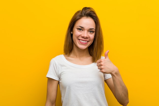 Jovem mulher caucasiana natural sorrindo e levantando o polegar