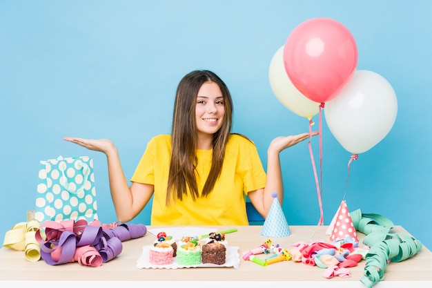 Jovem mulher caucasiana, organizando um aniversário faz escala com os braços, sente-se feliz e confiante.