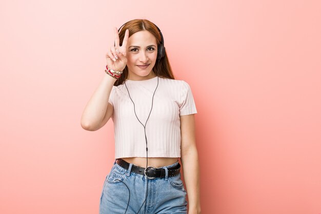 Jovem mulher caucasiana ouve música mostrando sinal de vitória e sorrindo amplamente.