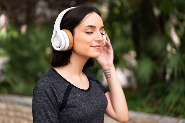 Jovem mulher caucasiana ouvindo música ao ar livre em um parque