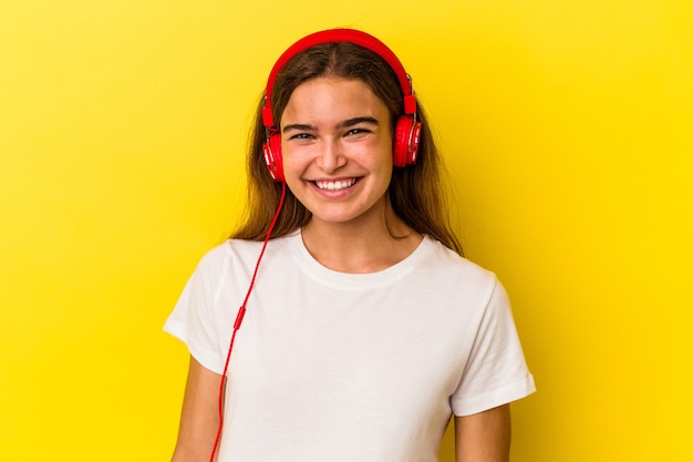 Jovem mulher caucasiana, ouvindo música isolada em fundo amarelo, feliz, sorridente e alegre.