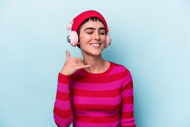 Jovem mulher caucasiana ouvindo música isolada no fundo, mostrando um gesto de chamada de celular com os dedos