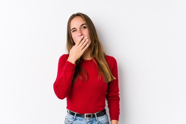 Jovem mulher caucasiana posando bocejando mostrando um gesto cansado, cobrindo a boca com a mão.