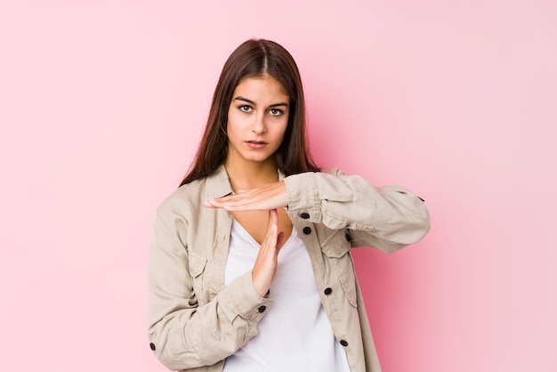 Jovem mulher caucasiana, posando em uma parede rosa, mostrando um gesto de tempo limite.