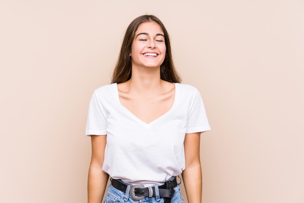 Jovem mulher caucasiana posando isolada ri e fecha os olhos, sente-se relaxada e feliz.