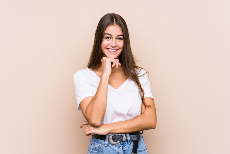 Foto jovem mulher caucasiana posando isolada sorrindo feliz e confiante, tocando o queixo com a mão.