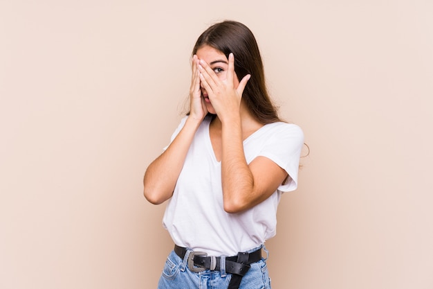 Jovem mulher caucasiana posando isolado piscar entre os dedos, assustada e nervosa.